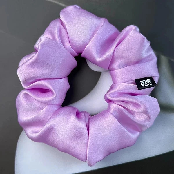 Lavender silk scrunchie displayed on a white stand against a gray background.