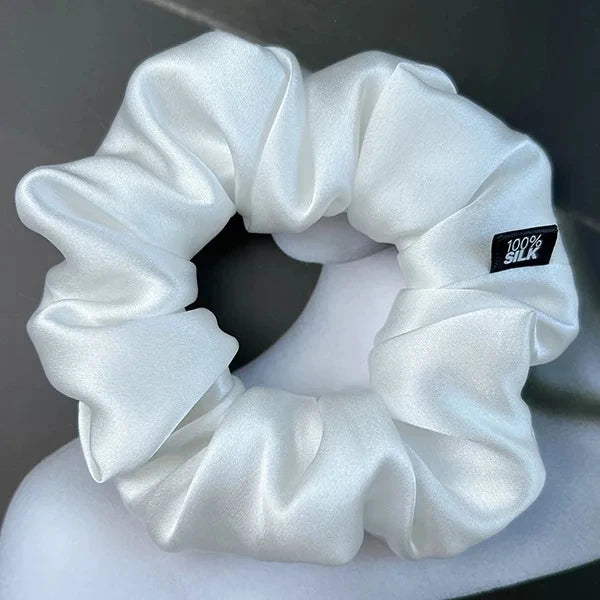 White silk scrunchie displayed on a white stand against a gray background.