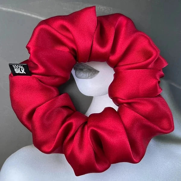 Red silk scrunchie displayed on a white stand against a gray background.