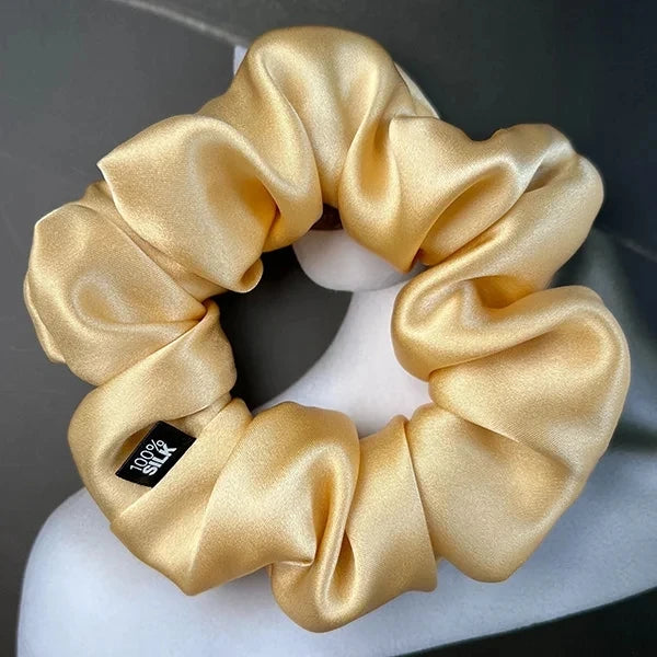 Gold silk scrunchie displayed on a white stand against a gray background.