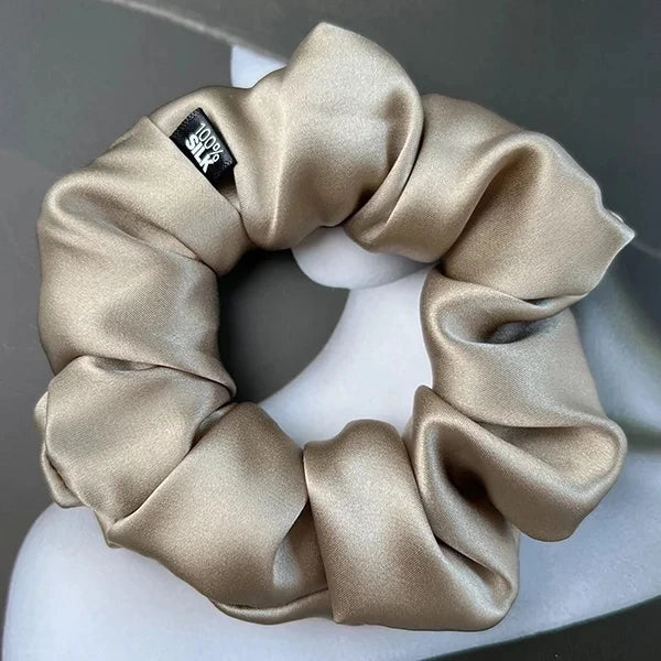 Champagne silk scrunchie displayed on a white stand against a gray background.