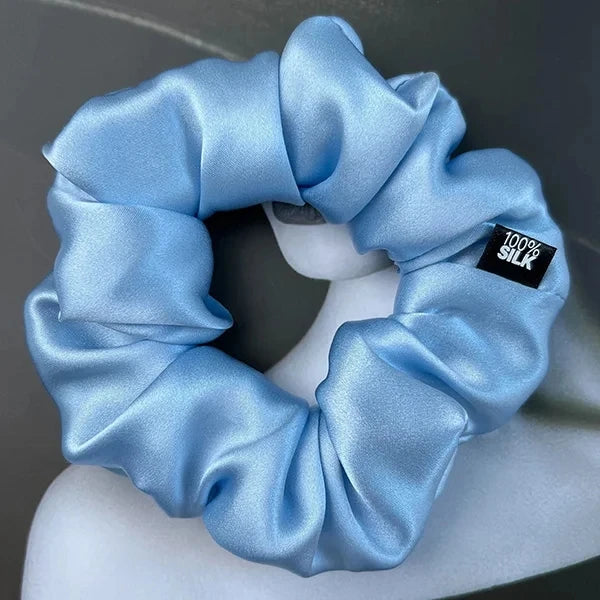 Baby blue silk scrunchie displayed on a white stand against a gray background.