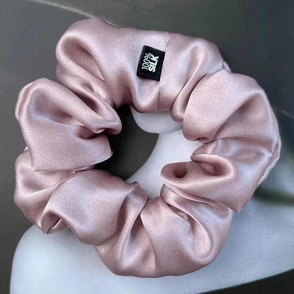 Pale mauve silk scrunchie displayed on a white stand against a gray background.