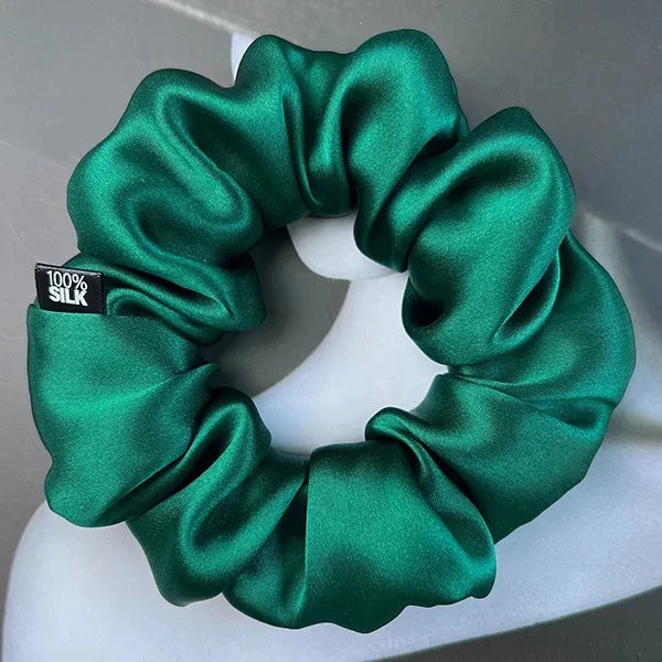 Emerald green silk scrunchie displayed on a white stand against a gray background.