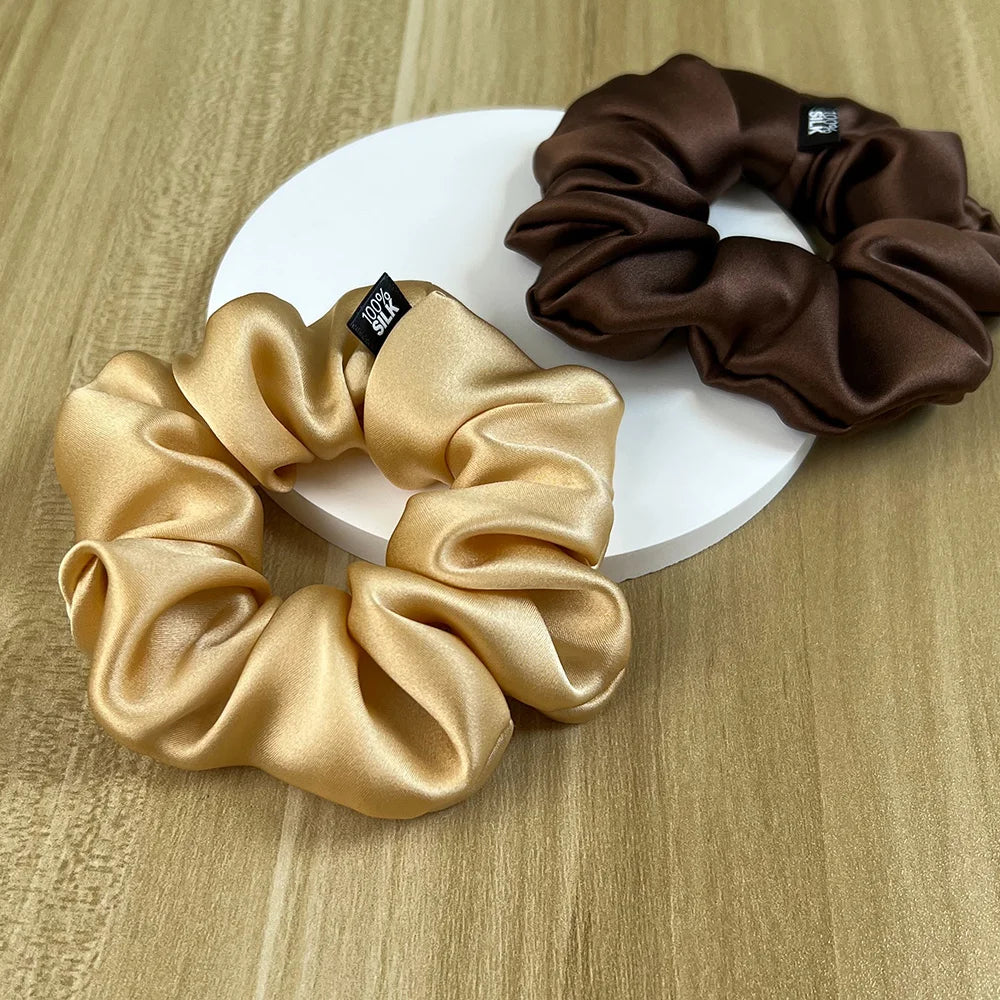 Gold and chocolate brown silk scrunchies arranged on a white display disc.