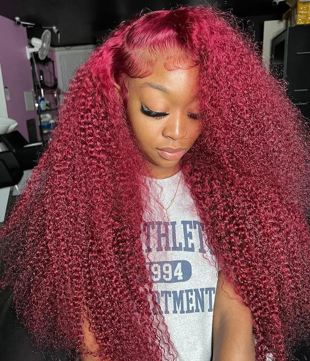 Model wearing a long burgundy water wave wig with voluminous curls, a side part and sculpted baby hairs.