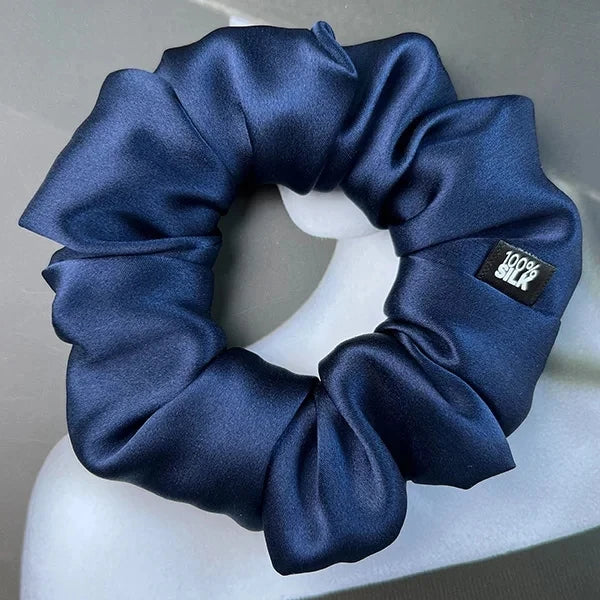 Navy blue silk scrunchie displayed on a white stand against a gray background.