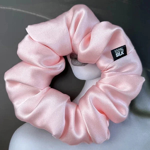 Pale pink silk scrunchie displayed on a white stand against a gray background.