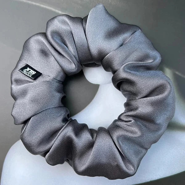Gray silk scrunchie displayed on a white stand against a gray background.