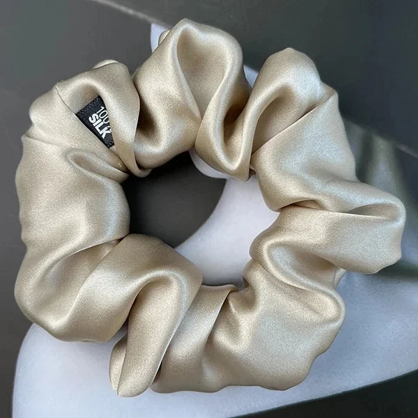Light champagne silk scrunchie displayed on a white stand against a gray background.
