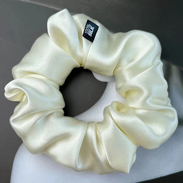 Ivory silk scrunchie displayed on a white stand against a gray background.