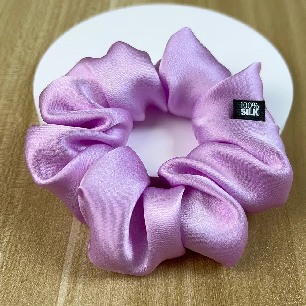 Lavender silk scrunchie with glossy gathered folds on a wooden surface.