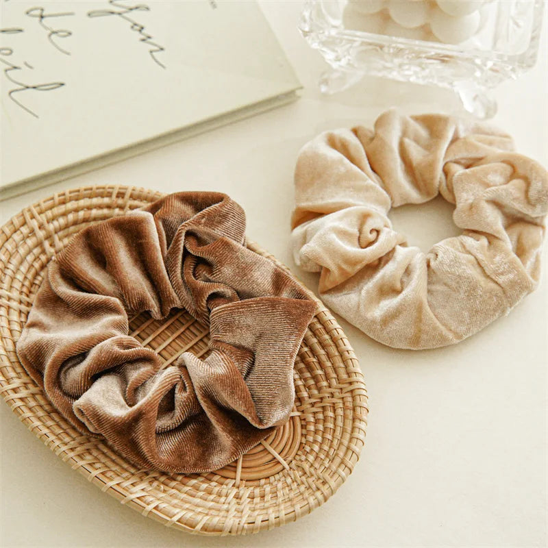 Coffee velvet scrunchie on a woven tray beside a beige velvet scrunchie