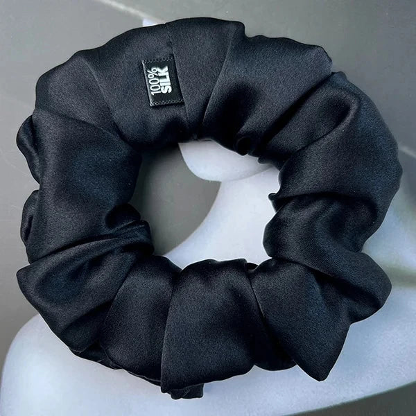 Black silk scrunchie displayed on a white stand against a gray background.