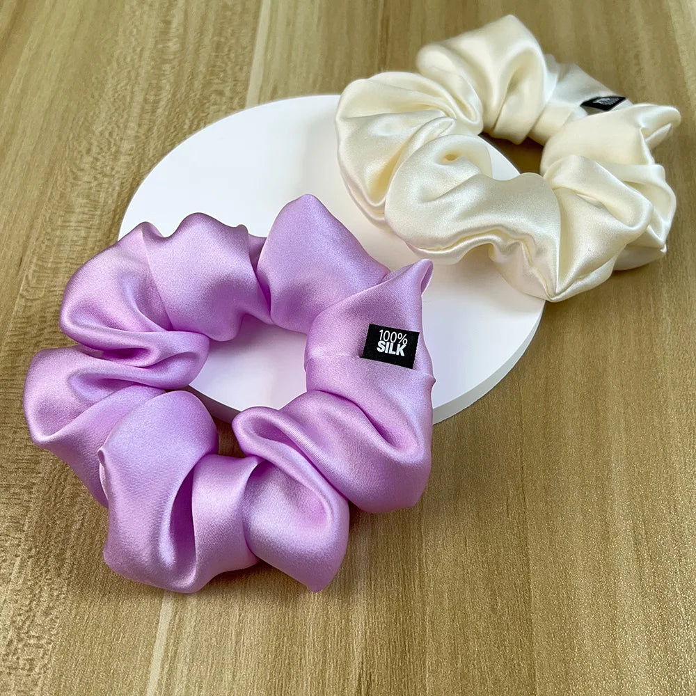 Lavender and ivory silk scrunchies arranged on a white display disc on a wooden surface.