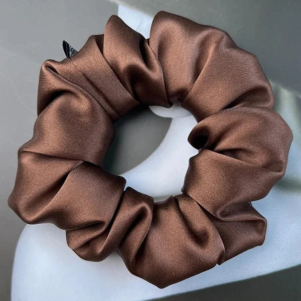 Chocolate brown silk scrunchie displayed on a white stand against a gray background.