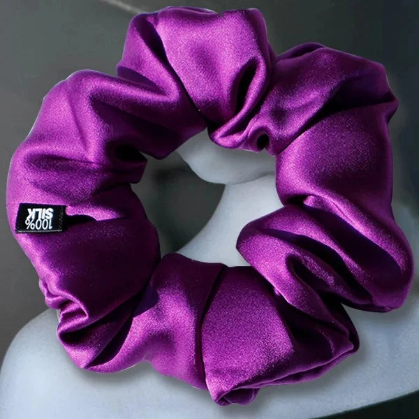Deep purple silk scrunchie displayed on a white stand against a gray background.