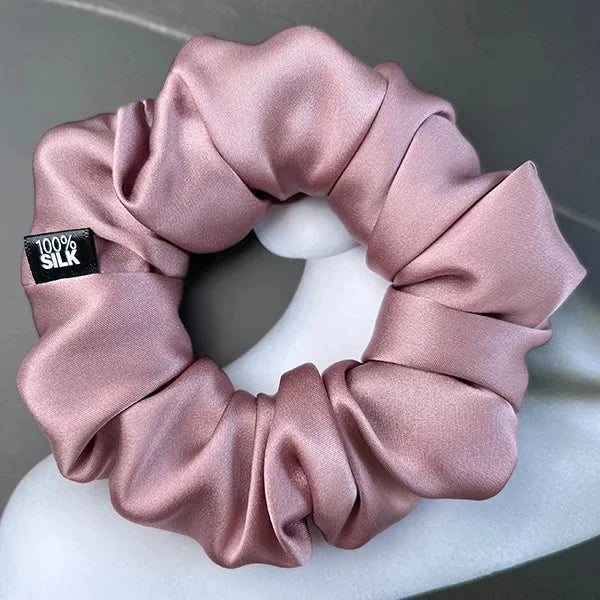 Dusty rose silk scrunchie displayed on a white stand against a gray background.